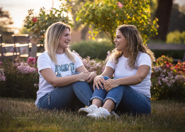 Zwei Frauen sitzen lachend im Park auf dem Gras.