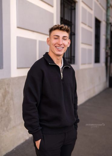 Junger Mann in schwarzem Pullover lächelt.