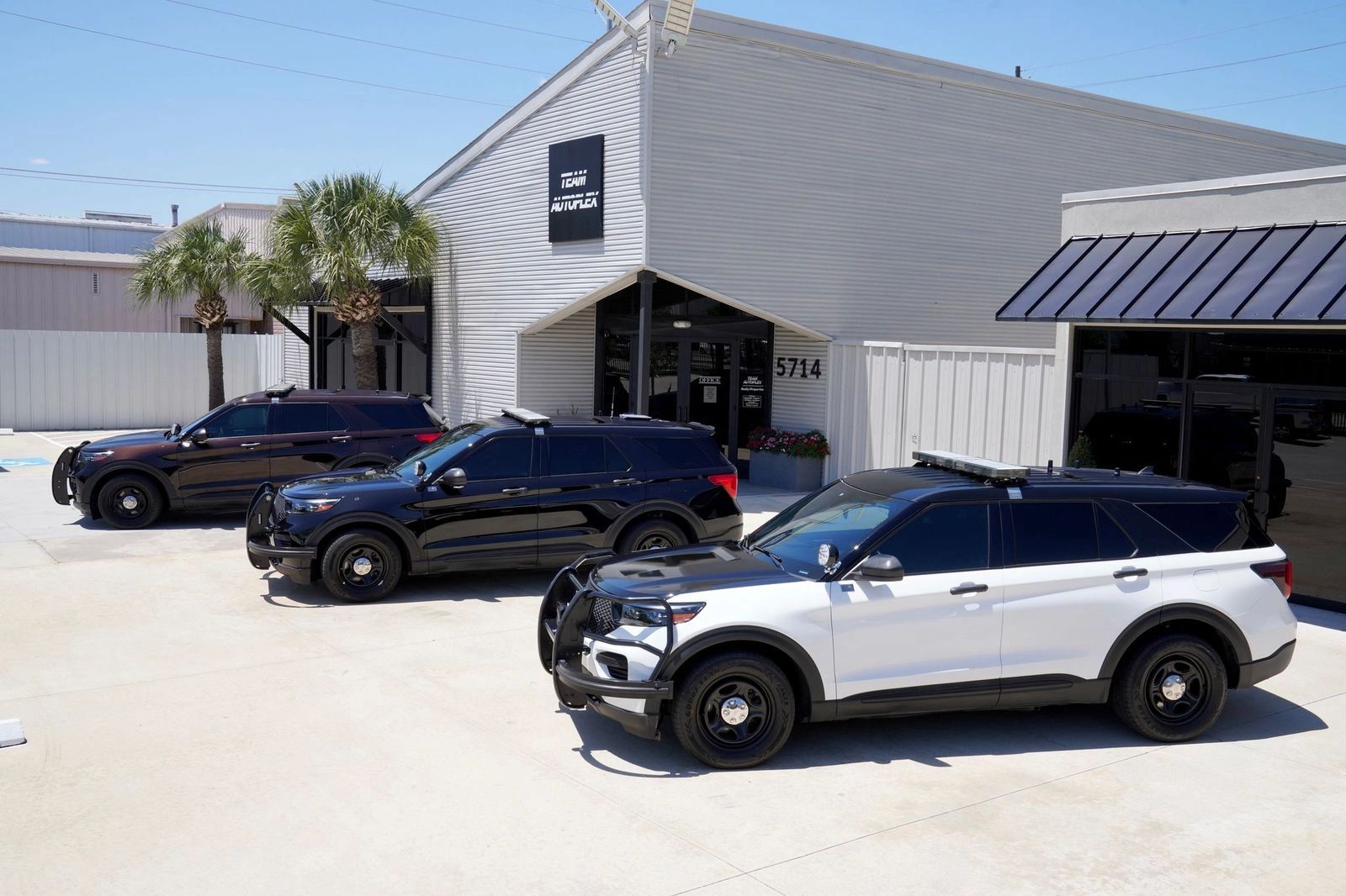 Three police SUVs parked outside a white building under clear skies.
