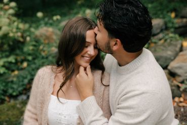 Man kissing woman on forehead outdoors.