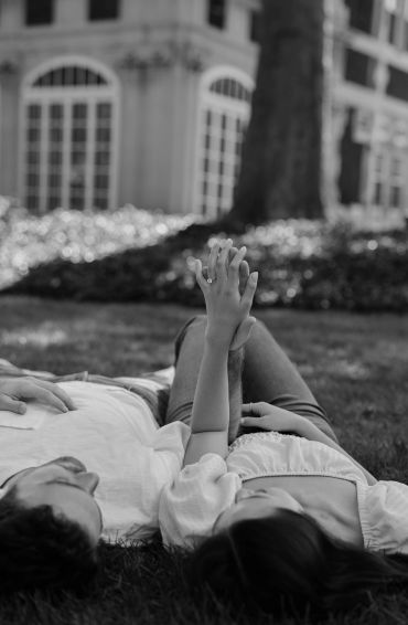 Couple lying on grass holding hands in black and white.