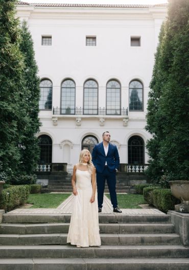 Couple posing elegantly in front of a grand white building.