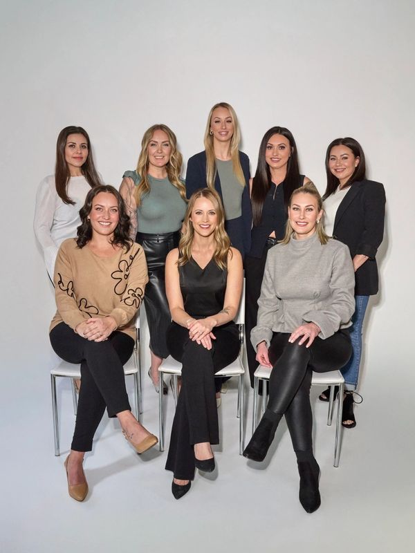 Group of eight women posing in a studio with a white backdrop.