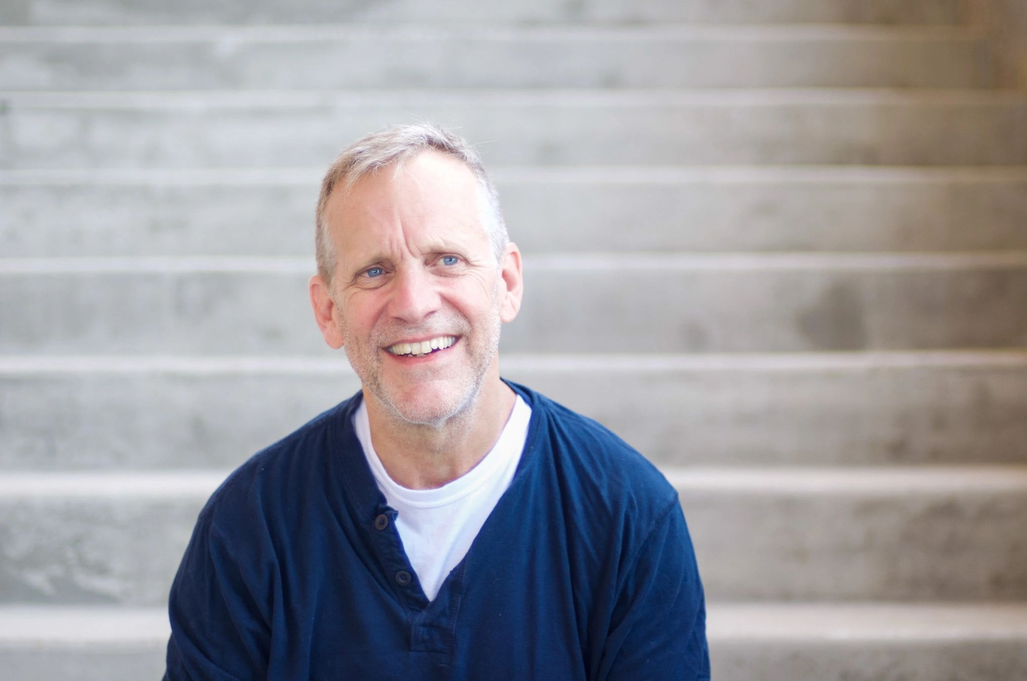 Smiling man with blue eyes sitting in front of concrete steps.