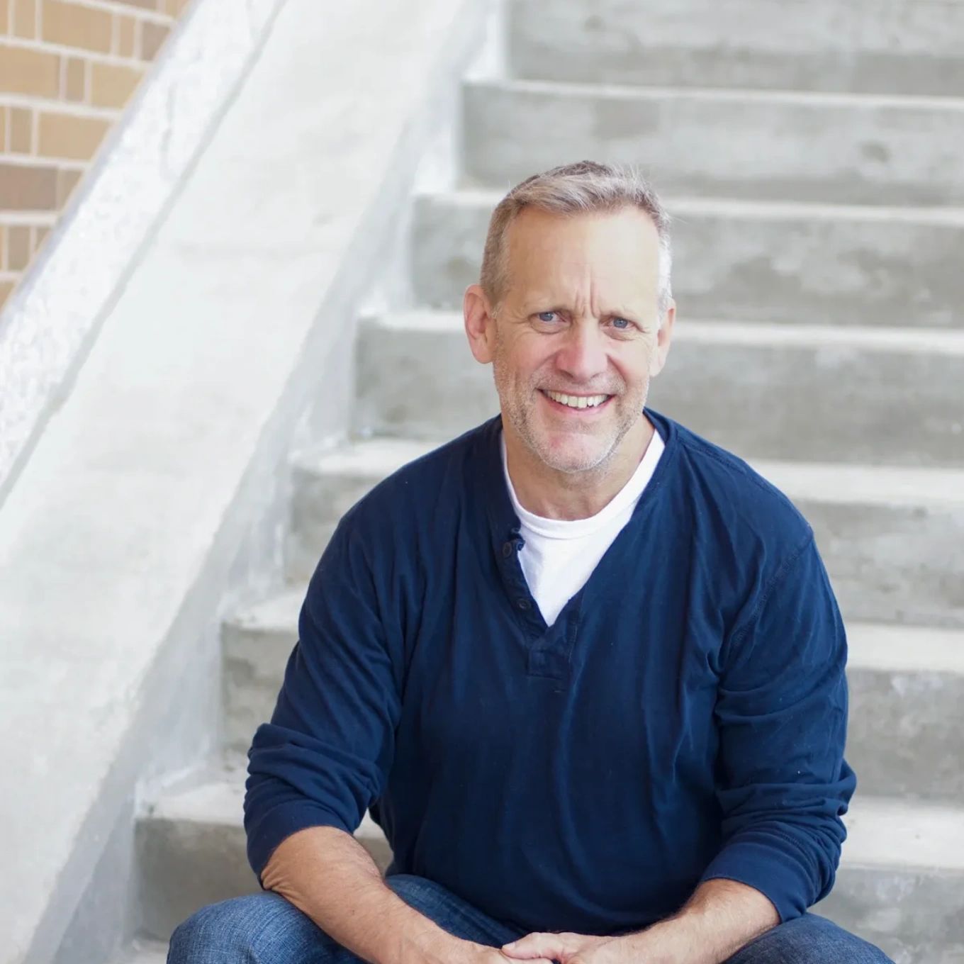 Smiling man sitting on concrete stairs wearing a navy blue shirt.