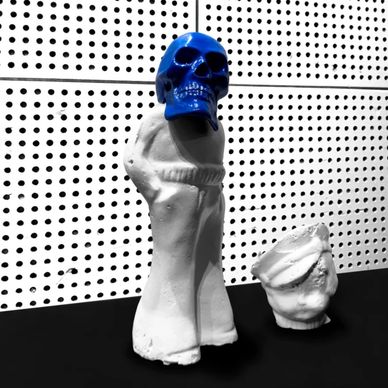 Sculpture with blue skull and white body, next to a small bust.