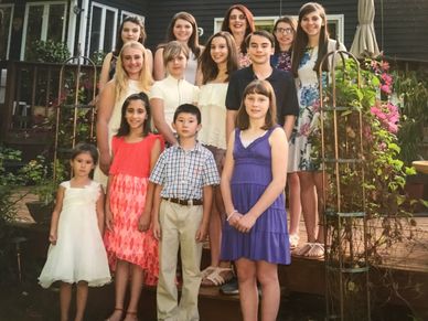 A group of children and teenagers posing outdoors in dresses and casual clothes.