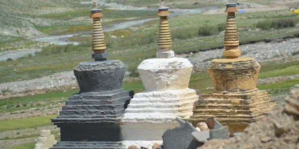 Three ancient stone stupas of different colors in a natural landscape.