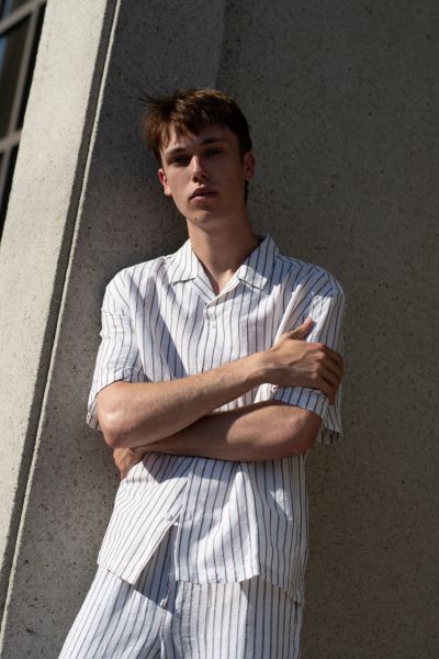 Young man posing against a concrete wall in striped attire.