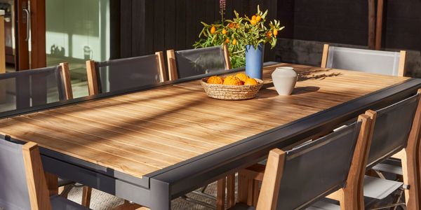 Sunlit teak and aluminum patio dining table with citrus on table surrounded by teak chairs.