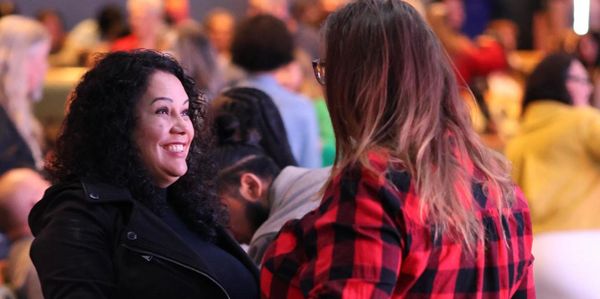 Two women engaged in a lively conversation at a crowded event.