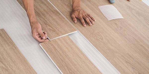 Hands installing wood-like vinyl flooring on a flat surface.
