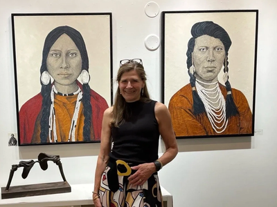 Woman standing in front of two Native American portrait paintings in an art gallery.