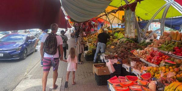 Busy outdoor market with colorful fruit stalls and shoppers walking.