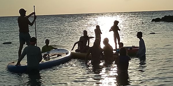 People enjoying paddleboarding and swimming at sunset on the water.