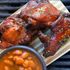 Delicious grilled chicken ribs with a smoky glaze, presented alongside beans on a grill
