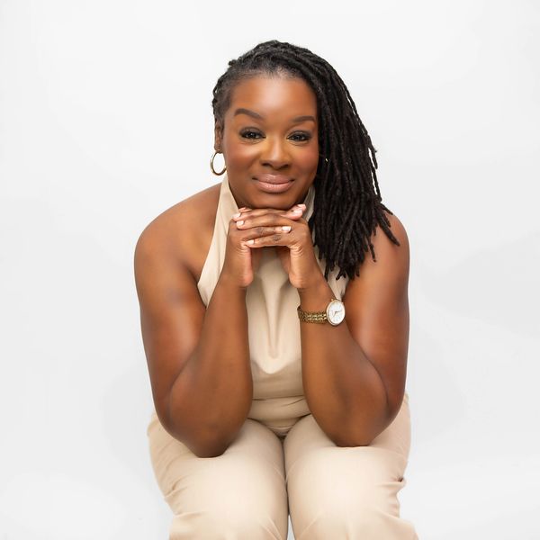 Confident woman with dreadlocks smiling, resting her chin on her hands.