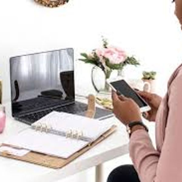 Person using phone at a desk with laptop and planner.