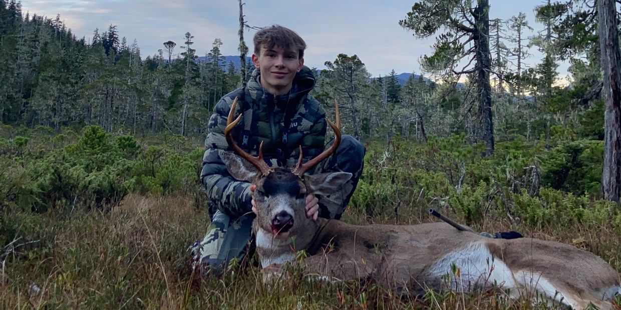 Young hunter posing with a deer in forest.