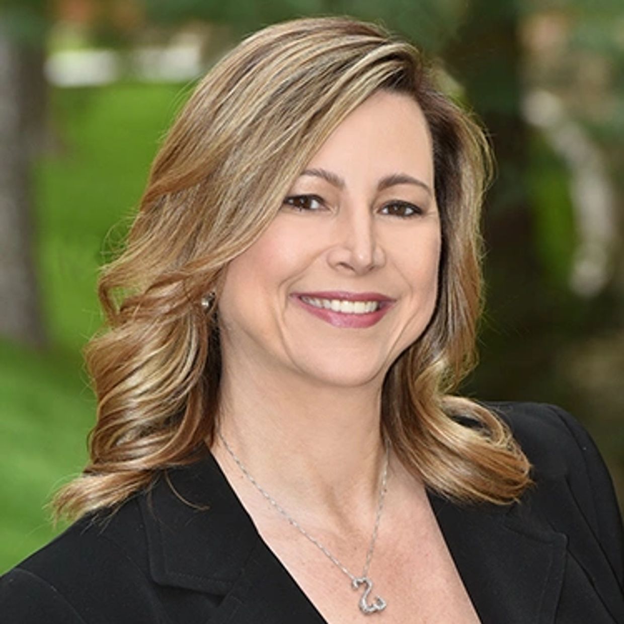 Smiling woman with blonde hair outdoors in professional attire.