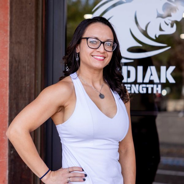 Smiling woman in athletic wear standing confidently outside a gym.