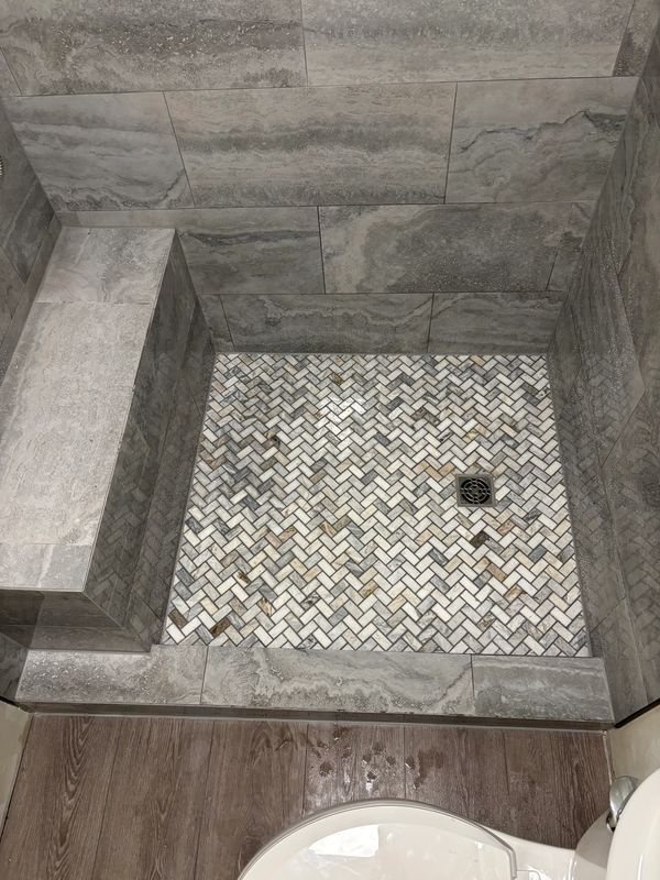 Modern shower with gray stone walls and herringbone patterned floor tiles.