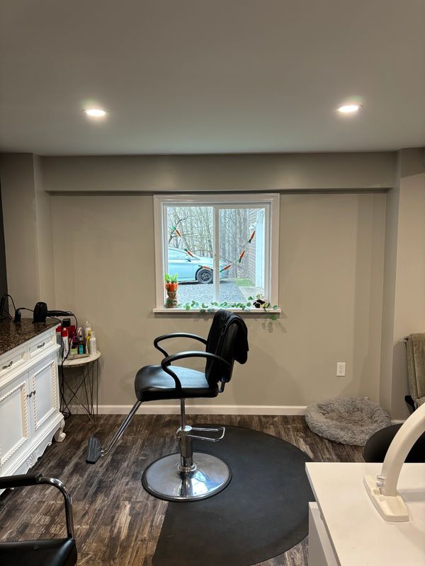 Black salon chair in front of a window with a car outside and cozy decor.