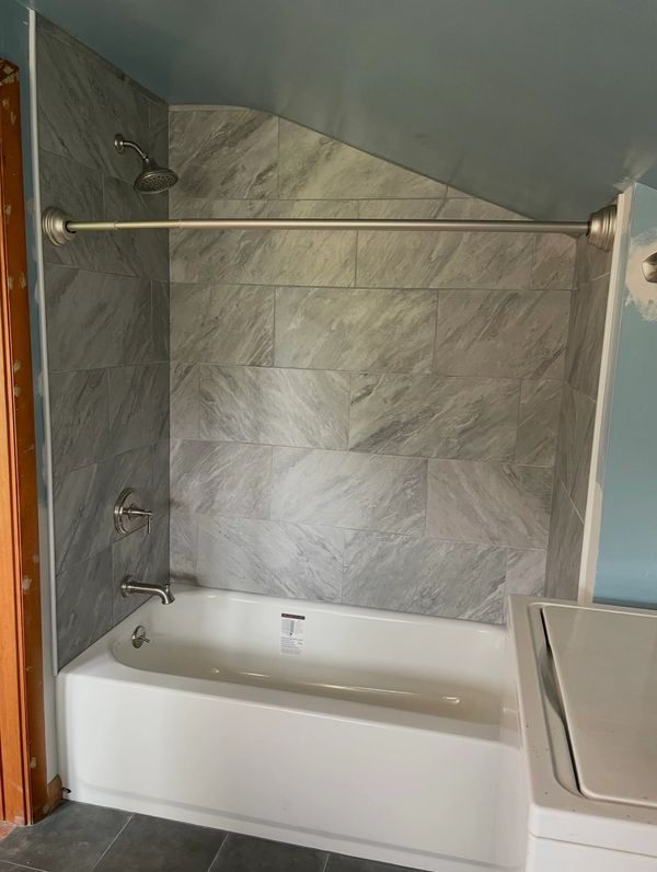 Newly installed bathtub with gray tiled walls and silver fixtures.