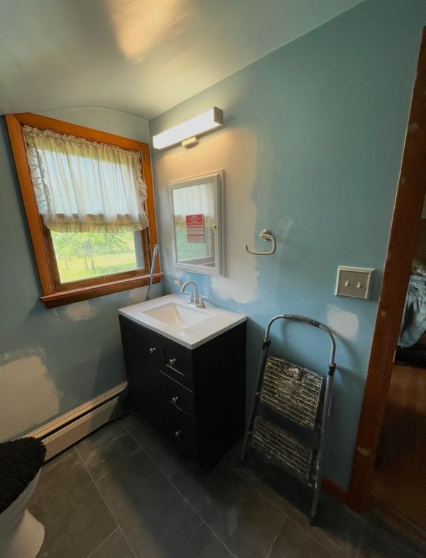 Bathroom with a dark vanity, window, and step ladder against partially painted blue walls.