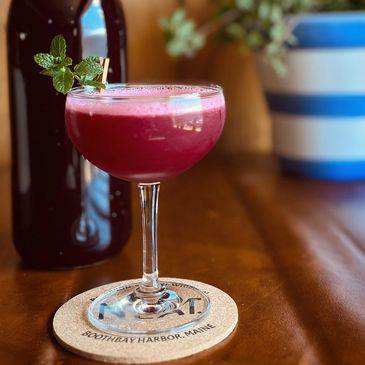 A red cocktail made with beets sits on a table. The drink is garnished with fresh mint.