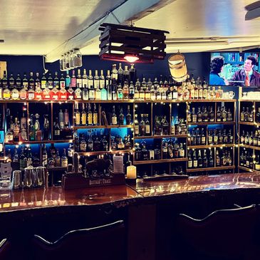 Shelves stocked with over 300 bottles of different whiskies. The bar top is made of live-edge wood.