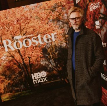 A man stands in front of an HBO Original Rooster promotional backdrop.