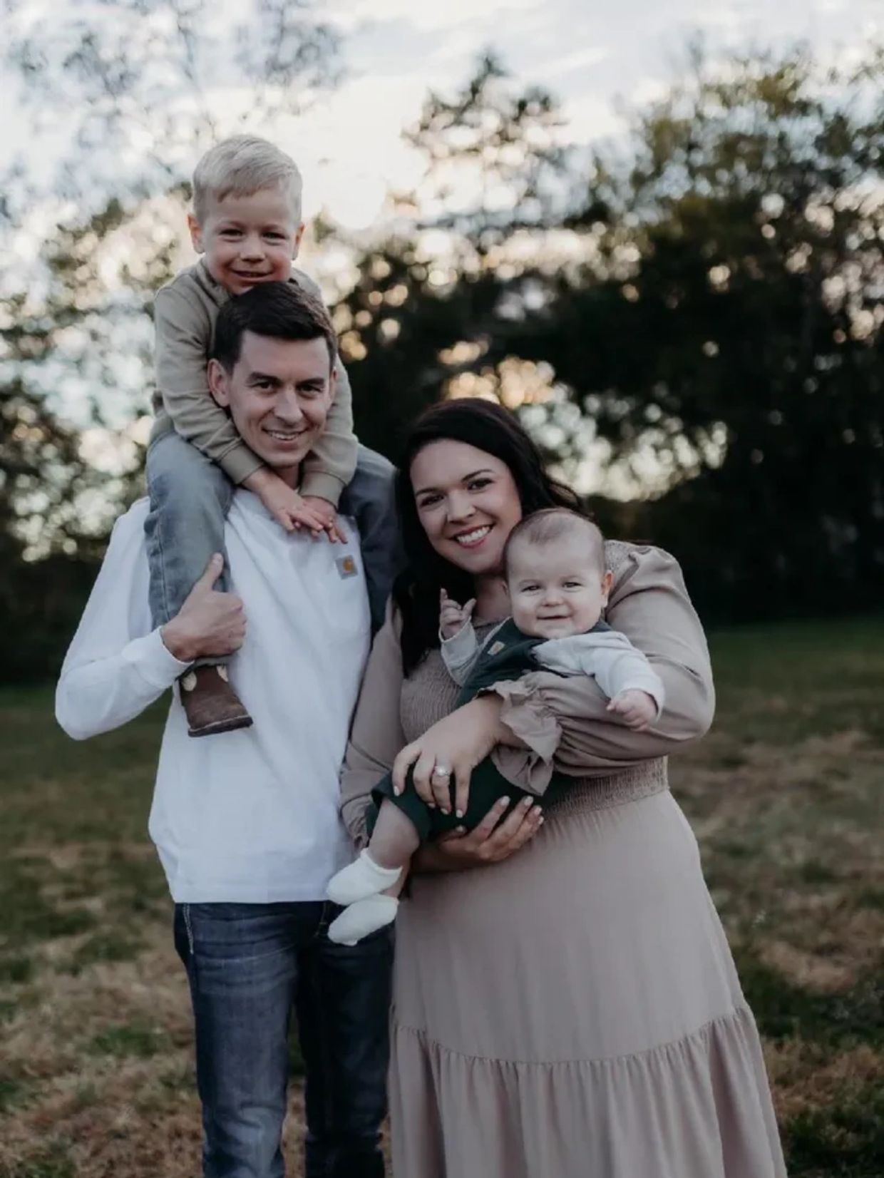 A happy family with two children posing outdoors during sunset.