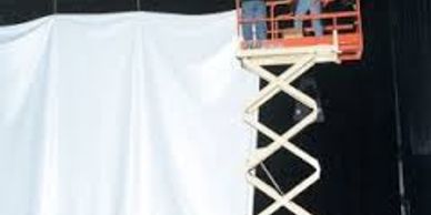 Workers on a scissor lift installing or working near a large white curtain.