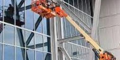A cherry picker lift outside a tall office building with glass windows.