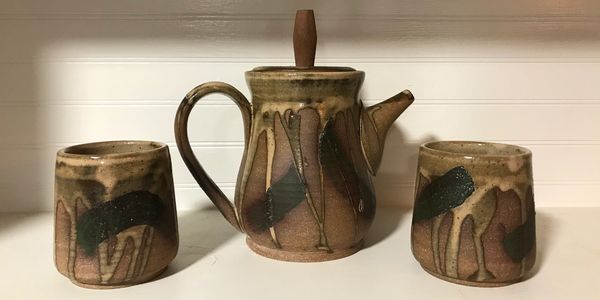 Rustic ceramic teapot with two matching cups on a white surface.