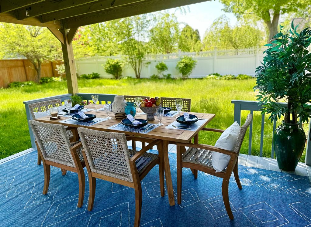 Outdoor dining table set for six on a covered patio with greenery.