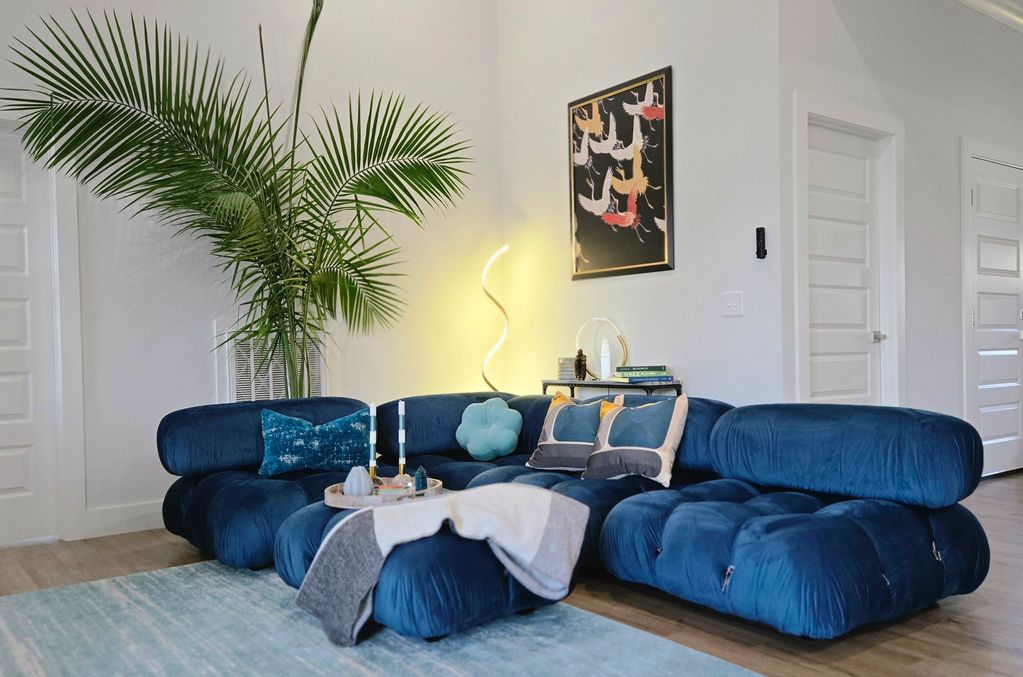 Modern living room with a plush blue sectional sofa and tall green plant.