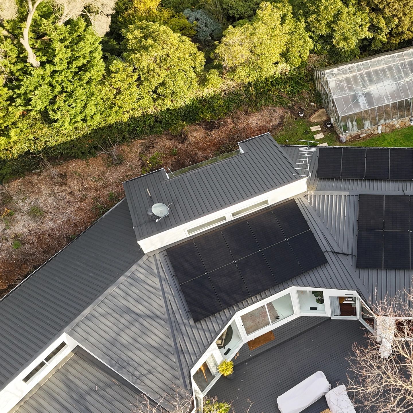 A modern house roof with solar panels and surrounding greenery.