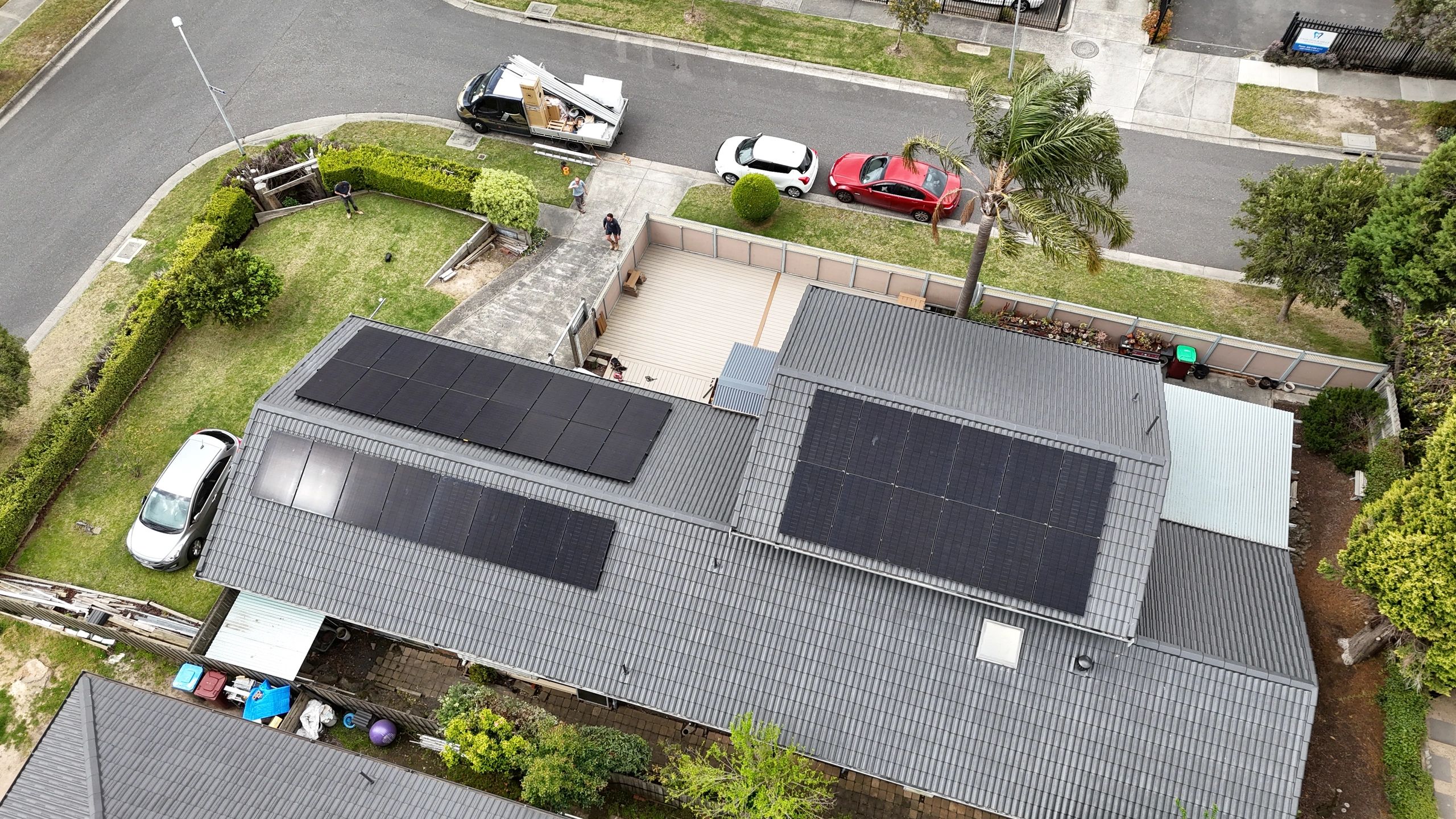 Aerial view of rooftops with solar panels and parked cars.