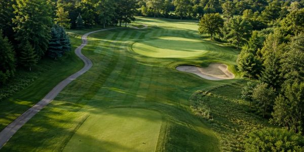Aerial view of a golf course fairway, green, sand bunker, and surrounding managed turf.