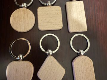 Six blank wooden keychains in different shapes on a wooden surface.