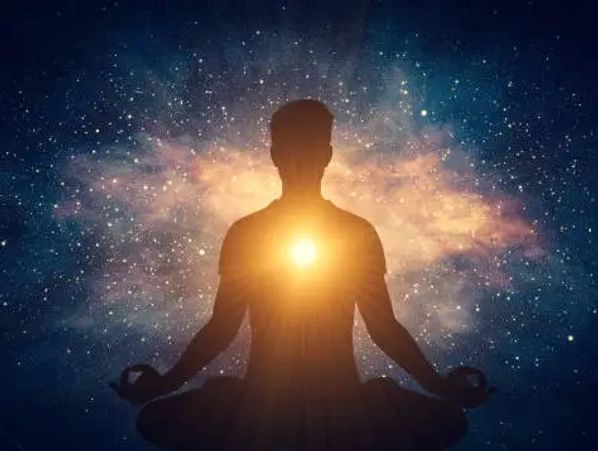 Silhouette of person meditating with glowing light at the heart against a cosmic background
