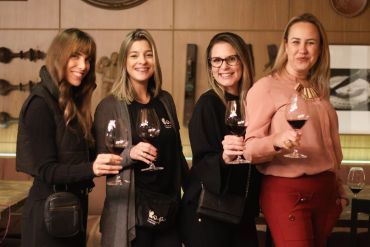Quatro mulheres brindando com vinho tinto.