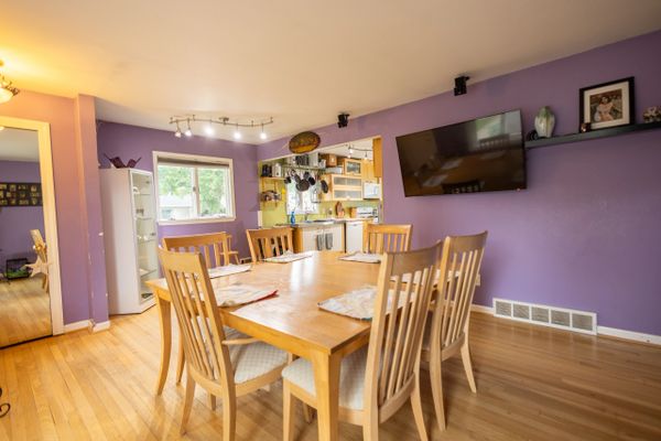 Bright dining area with wooden table and chairs, purple walls, and an open kitchen.