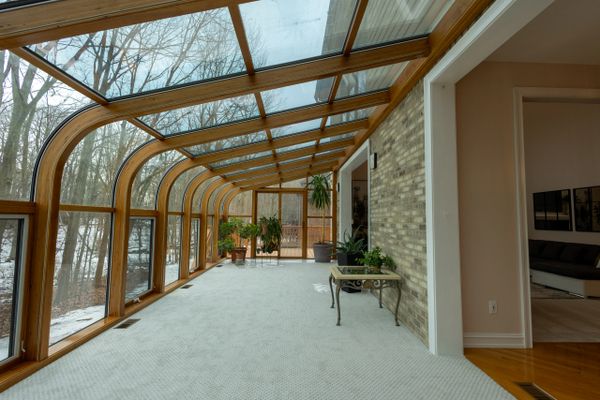 Sunroom with wooden frames and glass ceiling overlooking snowy trees.