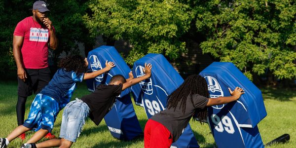Kids practicing football with coach outdoors.