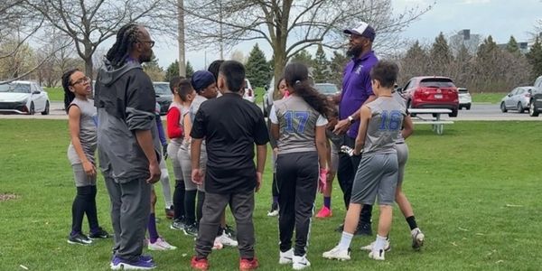 Kids and coaches chatting on a grassy field.