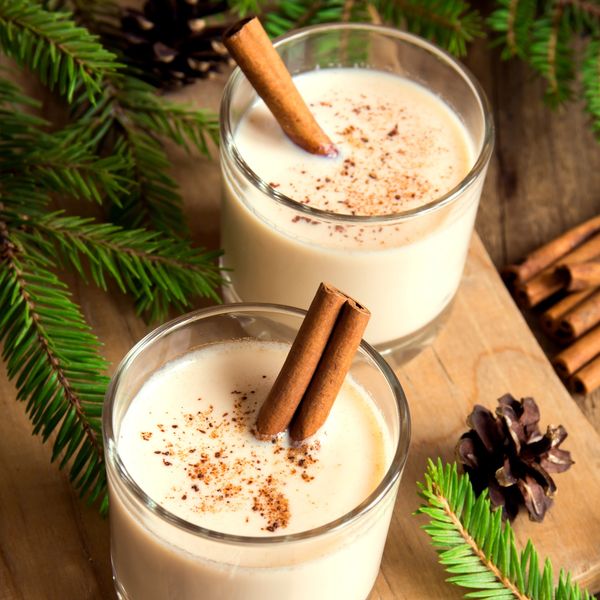 Two glasses of eggnog with cinnamon sticks and sprinkles.