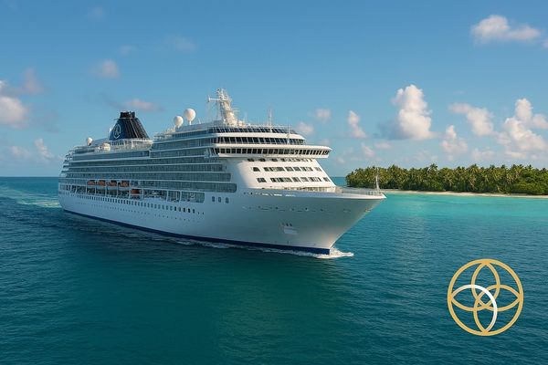 A large white cruise ship sailing near a tropical island under a blue sky.